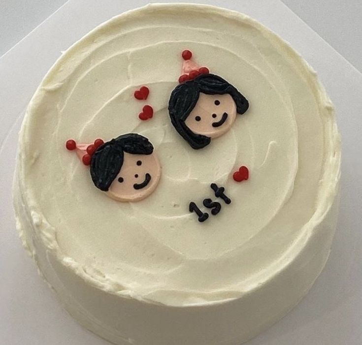 White minimalist cake with two edible fondant character faces wearing party hats and red hearts