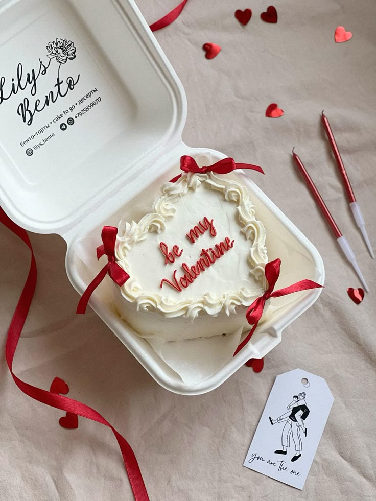 A white bento cake featuring a ruffled heart border, small red bows, and the text "be my Valentine".