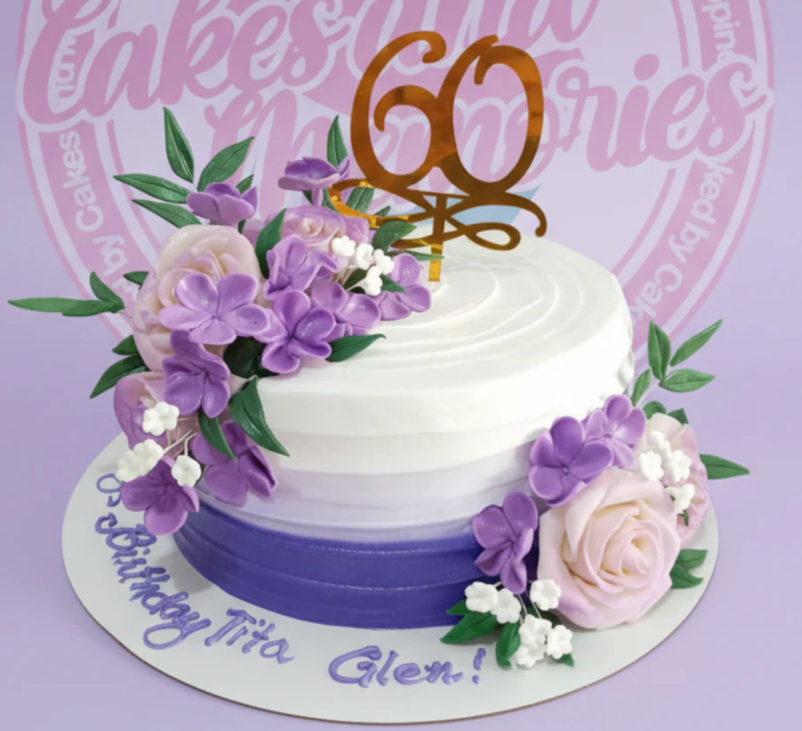 A white and purple ombre 1-tier cake decorated with realistic purple and pink gumpaste roses and a gold 60th birthday topper.
