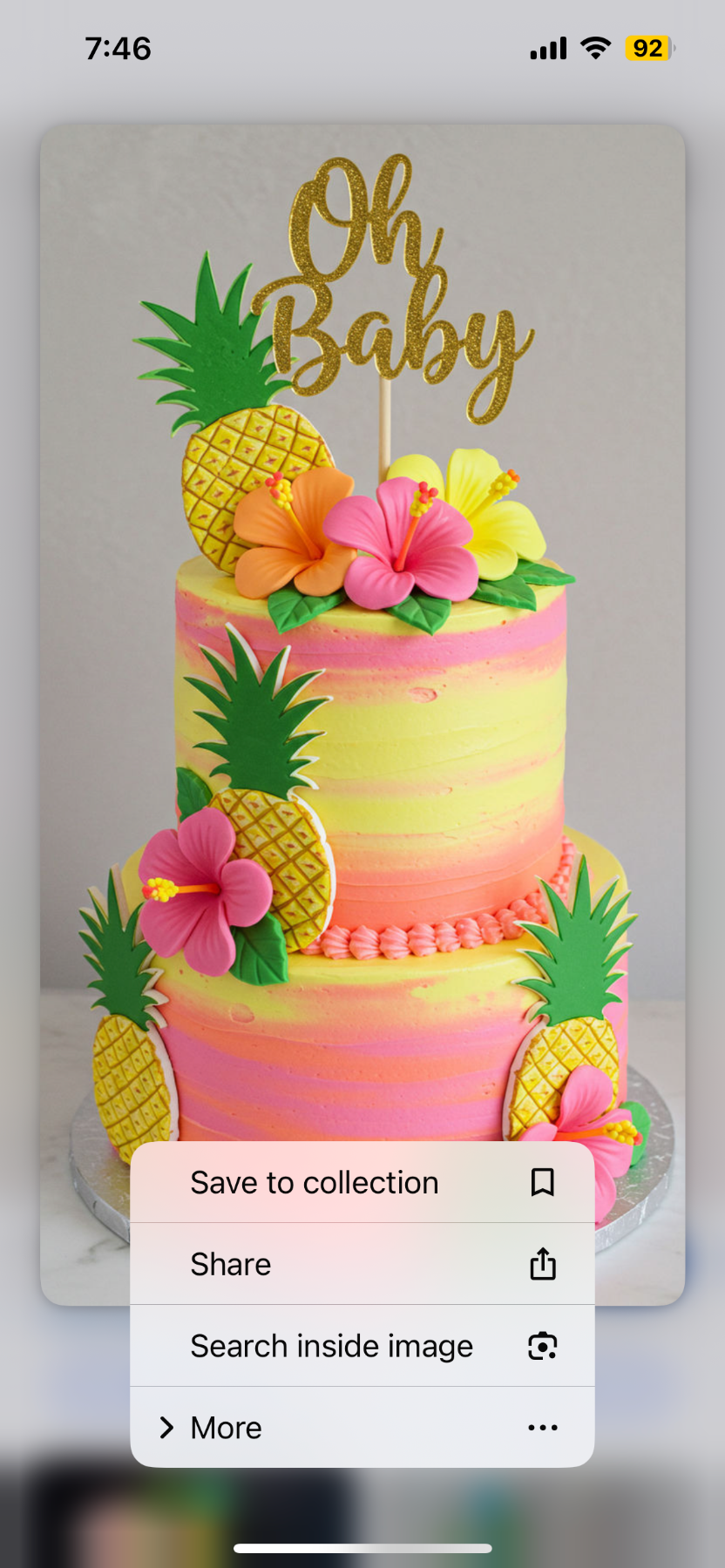 A vibrant 2-tier tropical themed cake with yellow and pink gradient icing, decorated with pink and orange hibiscus flowers and pineapple toppers.